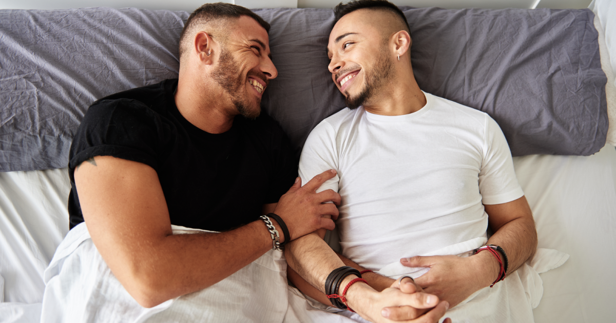 A loving gay couple embraces each other in bed, having overcome the blame game in their relationship through their successful experience at Loving at Your Best Marriage and Couples Counseling in New York, NY. Their newfound understanding and improved communication skills have deepened their connection and happiness.