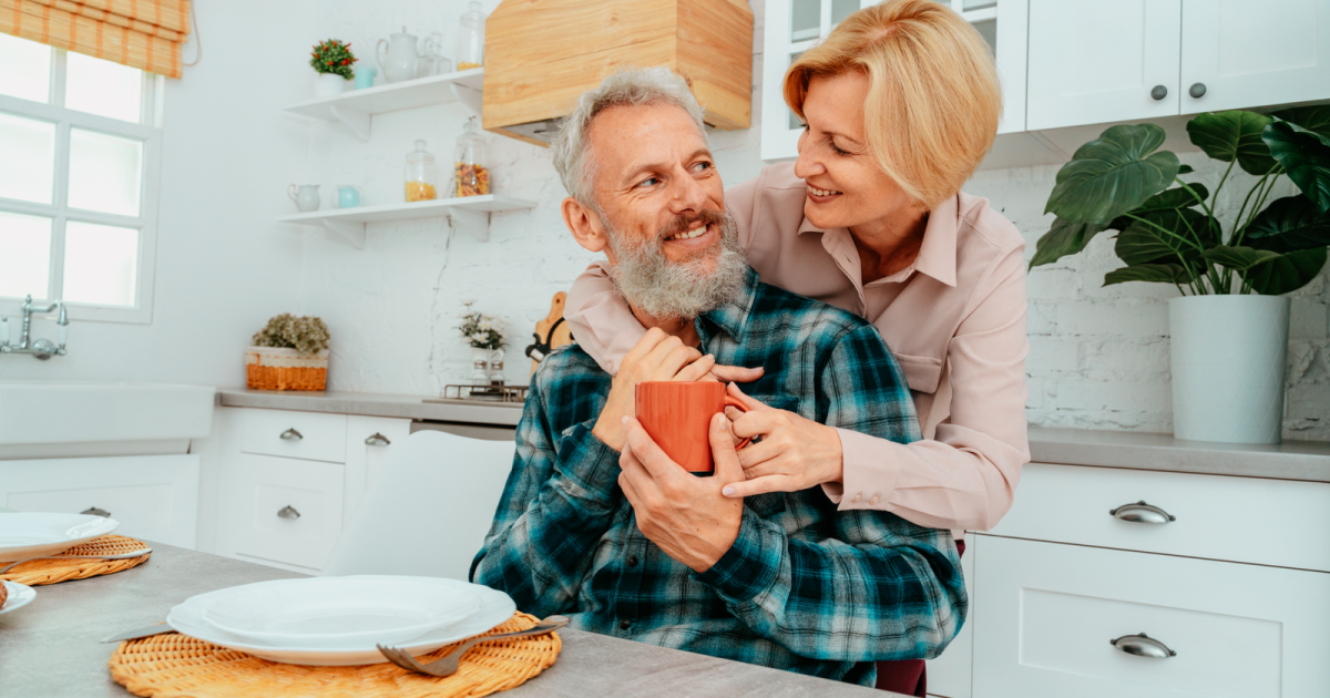 An older couple tenderly holds each other in their kitchen, having stopped the blame game in their relationship thanks to the successful marriage therapy they received at Loving at Your Best Marriage and Couples Counseling in New York, NY. Their renewed understanding and communication skills have brought them closer and reignited their love.